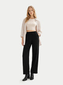Woman wearing a beige top, light pink cardigan, black pants, and black boots on a white background #color_off-white #ai-image