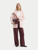 Woman holding a brown handbag wearing a light pink cardigan and dark red pants on a white background. #color_light-blush #ai-image