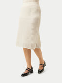 A woman wearing a beige knit cashmere skirt with an elasticated high-waist, paired with a white blouse with a sleeve detail.  #color_off-white