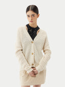 A woman wearing a beige cotton cashmere cardigan with a crew neckline and button closures over a black top and a beige skirt. #color_pure-white