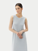 A woman standing in a studio setting, wearing a sleeveless, solid blue cashmere dress with a round neckline. #color_soft-ice