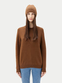 Person wearing a brown sweater and beanie with a plain background. #color_sepia-brown