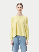 A woman wearing a yellow boatneck cotton silk cashmere blend sweater with long sleeves, paired with blue denim pants. #color_green-sheen