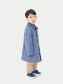 A child wearing a blue cashmere coat with buttons, over a white shirt and beige pants, standing against a white background. #color_deep-slate