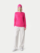 Person wearing a bright pink jumper and hat with white pants on a light grey background. #color_magenta-pink #ai-image