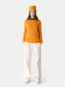 Person wearing an orange sweater, beanie, and white pants on a white background. #color_apricot-orange #ai-image