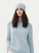 Woman wearing a light blue sweater and matching beanie against a white background #color_cloud-blue #ai-image