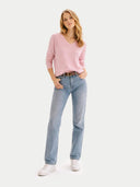 Woman wearing a pink v-neck sweater and light blue jeans on a white background #color_almond-blossom #ai-image