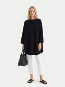 Woman wearing a black long-sleeve shirt and white pants, holding a black handbag on a white background. #color_black #ai-image