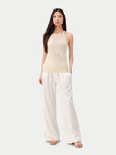 Woman wearing a beige sleeveless cashmere top and white pants on a white background. #color_off-white #ai-image