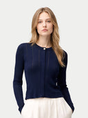 A woman modeling a navy blue ribbed knit cardigan with a single button closure, paired with white trousers, against a light gray studio background.#color_dark-indigo #ai-image