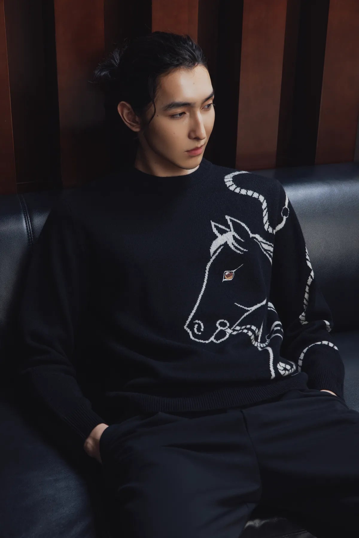 Man in a black cashmere sweater with a horse motif sitting on a leather seat | GOBI Cashmere